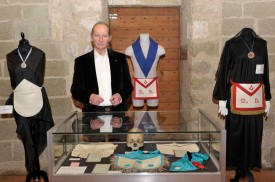 Michel Cugnet au milieu de tenues et objets de rite maçonniques exposés à l’Aula Magna du Château. © Michel Duperrex