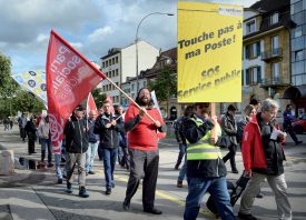 Armé de drapeaux et de pancartes, une dizaine de personnes ont scandé «Touche pas à ma Poste» dans les rues de la Cité thermale. ©Michel Duperrex