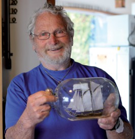 Jean de Bosset tenant l’un des nombreux bateaux en bouteille qu’il fabrique. ©Muriel Aubert